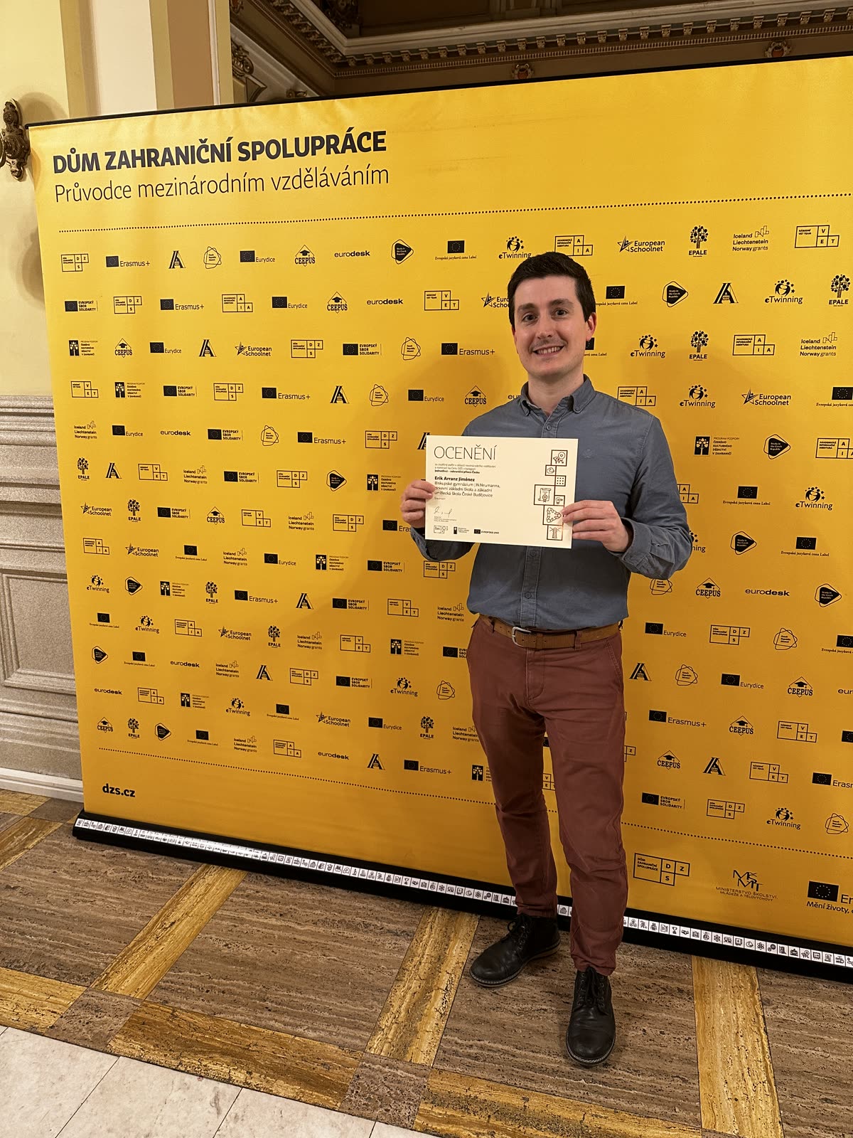 Erik Arranz Jiménez con el diploma de nominación delante del photocall amarillo del DZS en la gala de Praga
